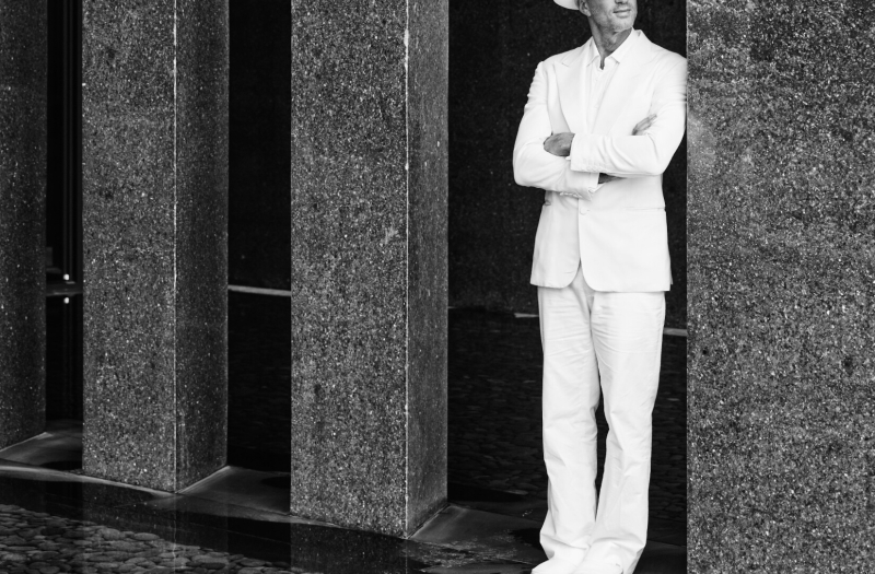 Alan Faena in all white leaning on a wall