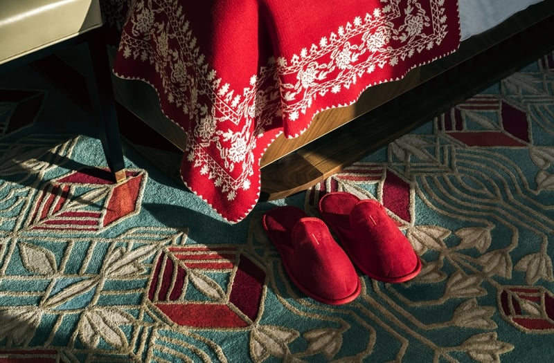A pair of red slippers on the floor next to a hotel bed