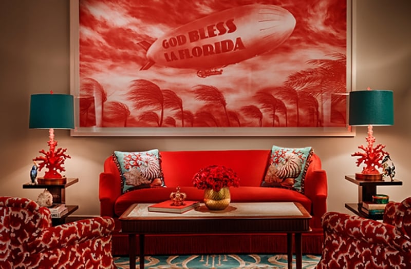 red couch sits between two teal lamps with a God Bless La Florida hung on the wall