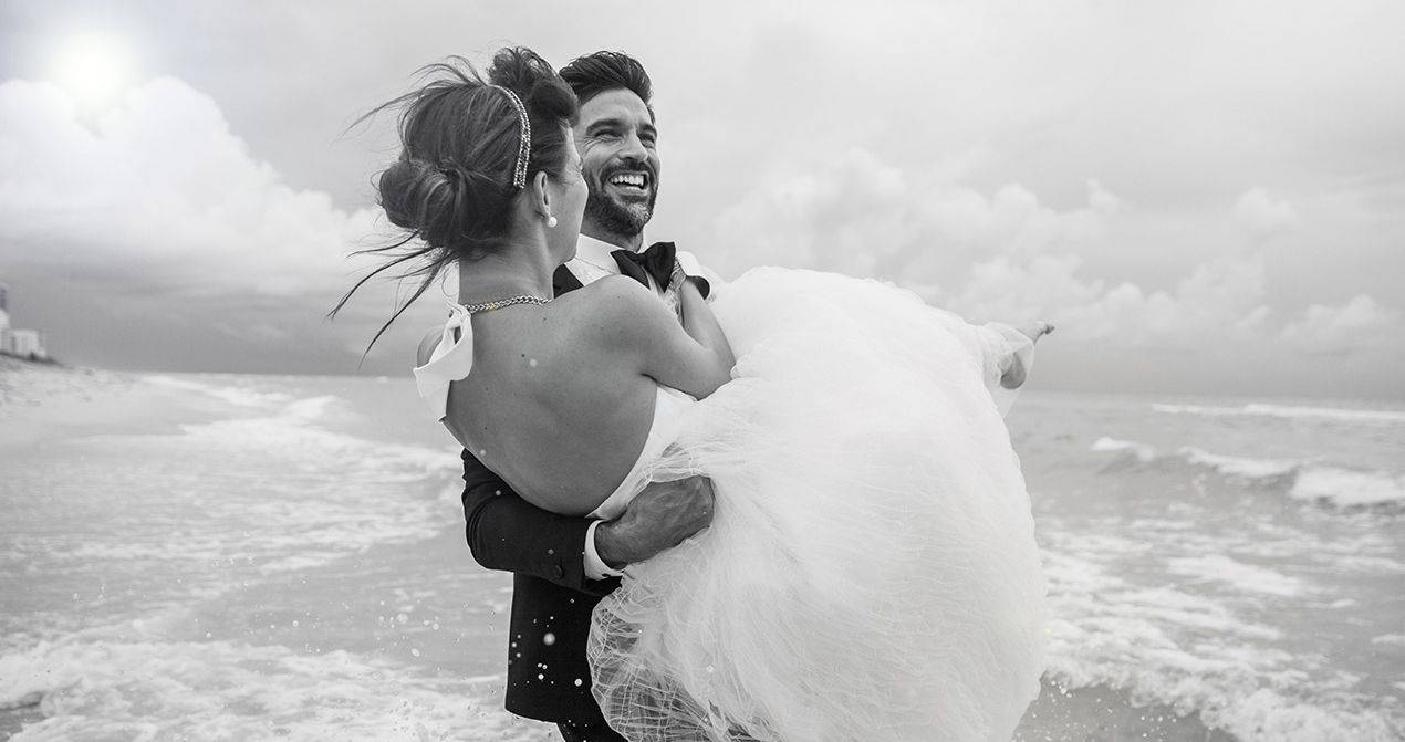 groom carries bride on the beach
