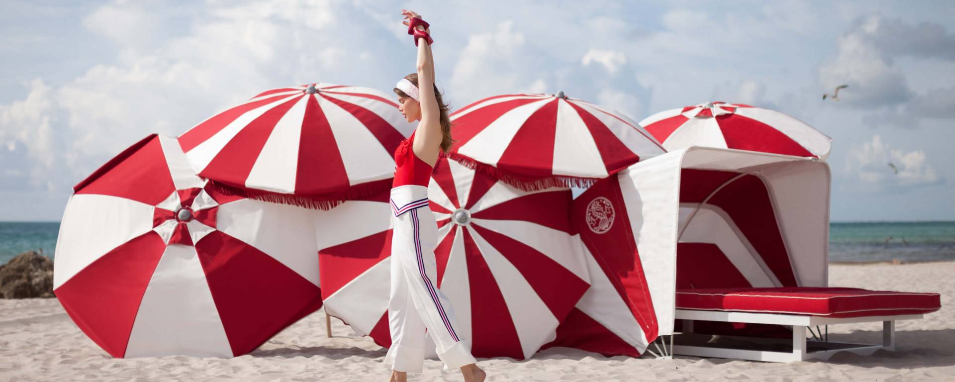 woman walking on the beach in front of red and white umbrellas