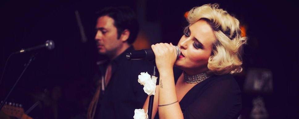 woman sings intro microphone while man plays guitar in background