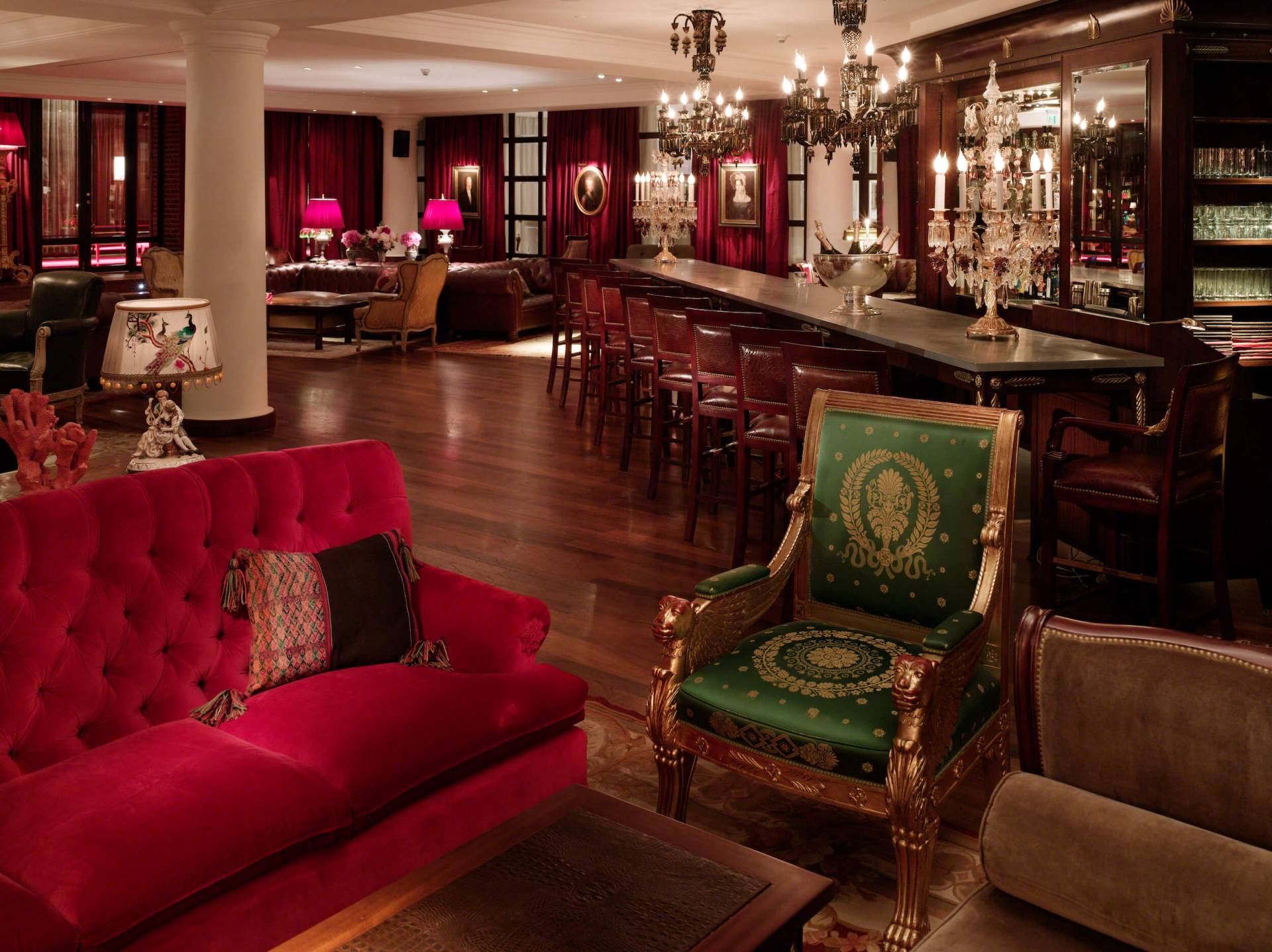 green chair and red couch sit in bar area with red curtains and chandeliers