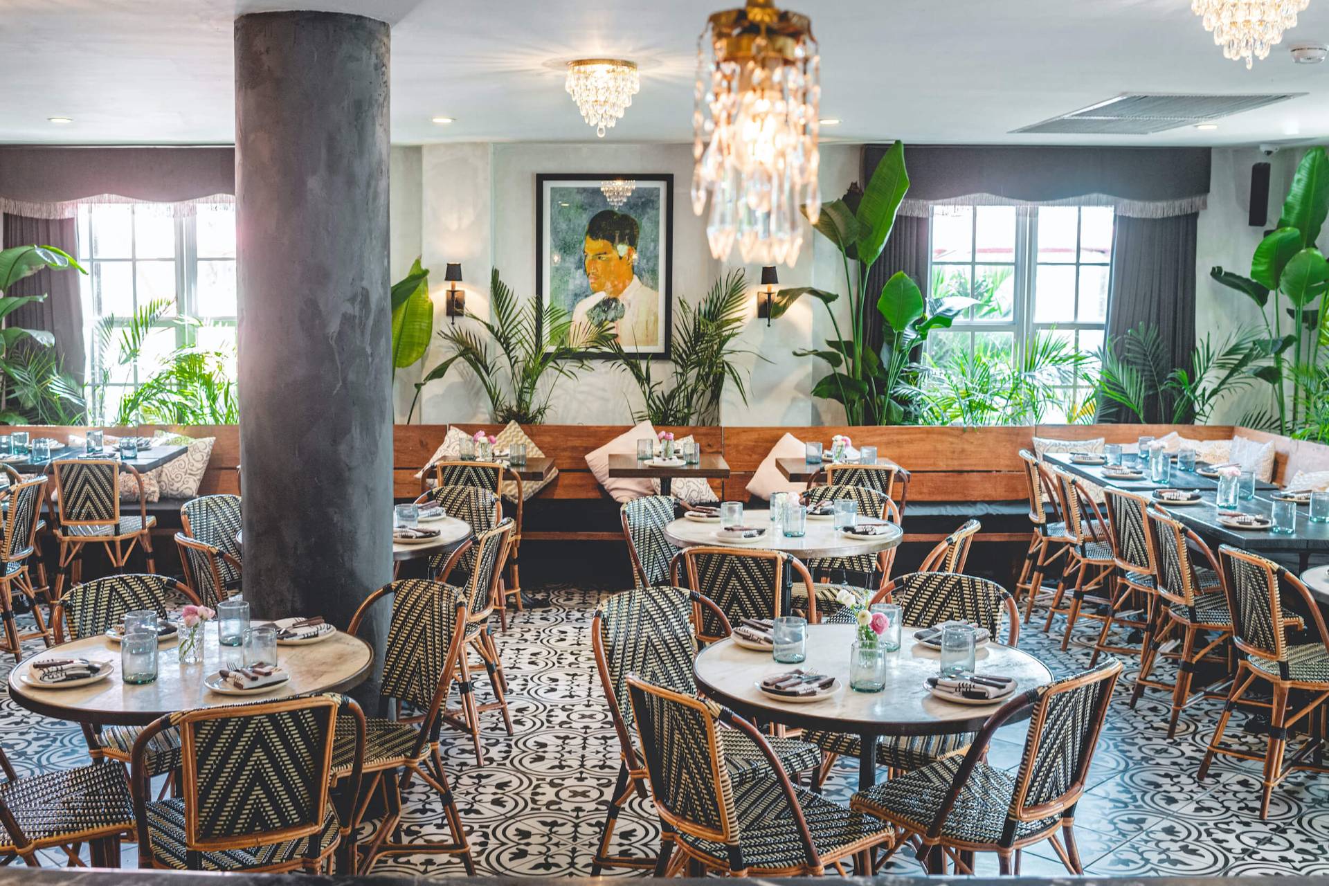striped chairs sit by round tables in a well-lit room with greenery near windows