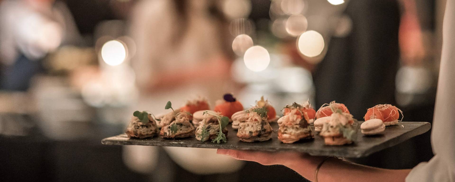 server with slate tray of appetizers walks toward two people blurry in background