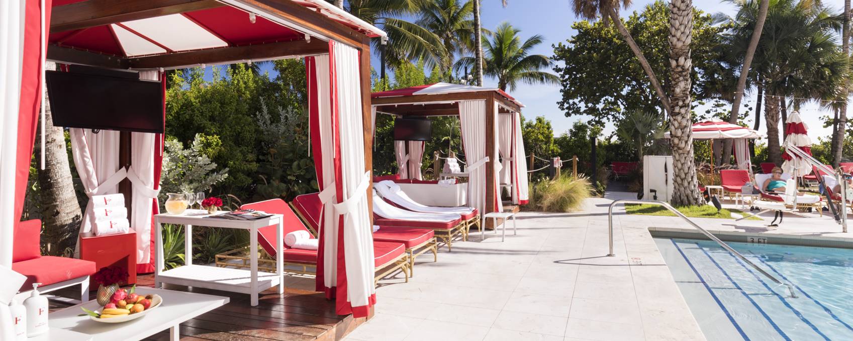 red and white tents sit poolside with openings show white and red seating underneath