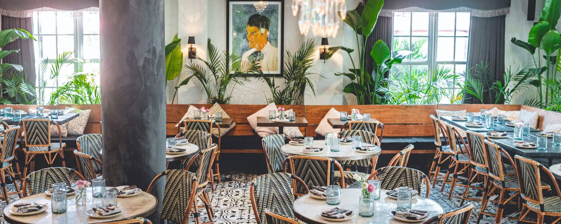 striped chairs sit by round tables in a well-lit room with greenery near windows