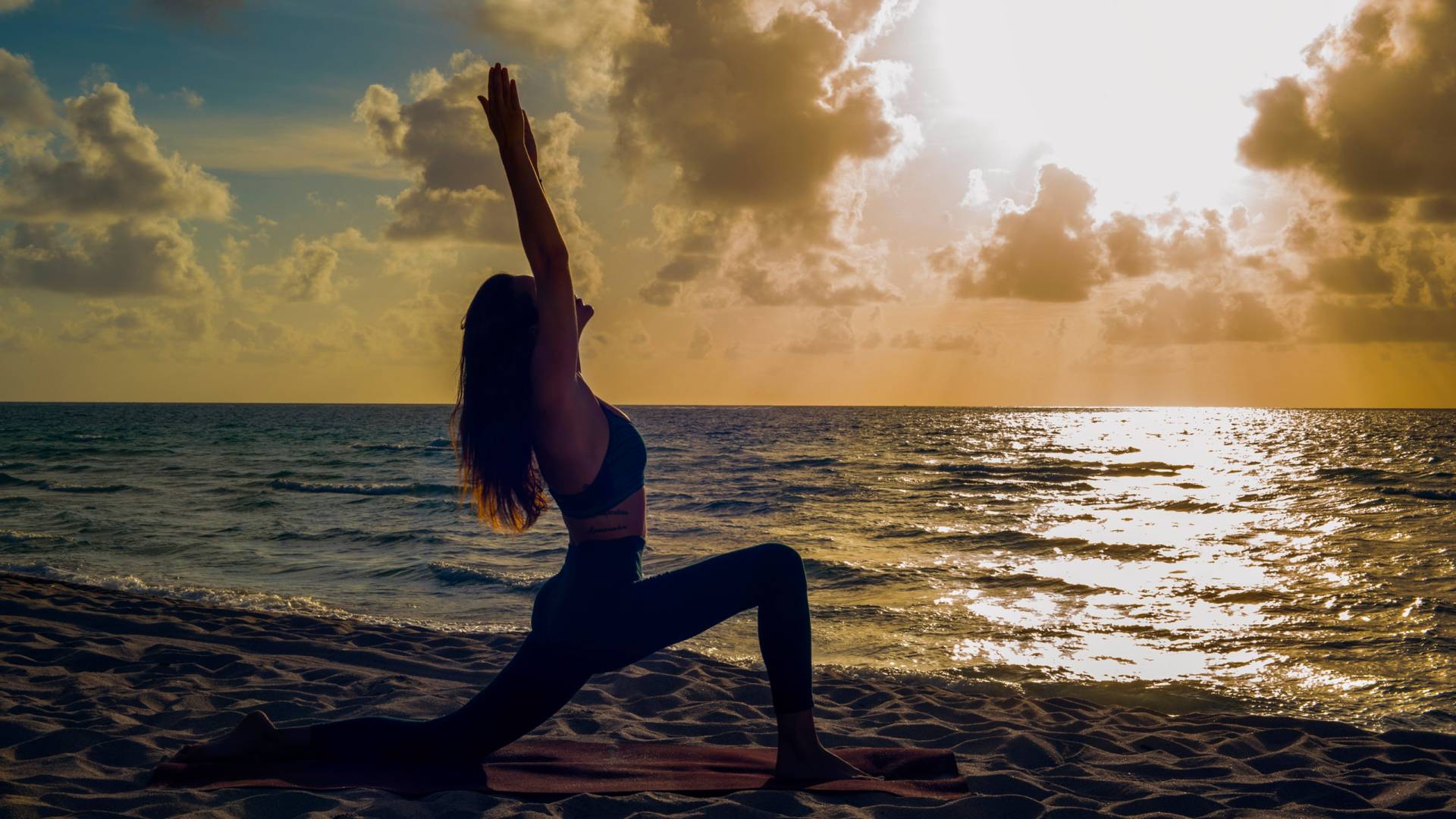 woman in silhouette performs a yoga pose on the beach