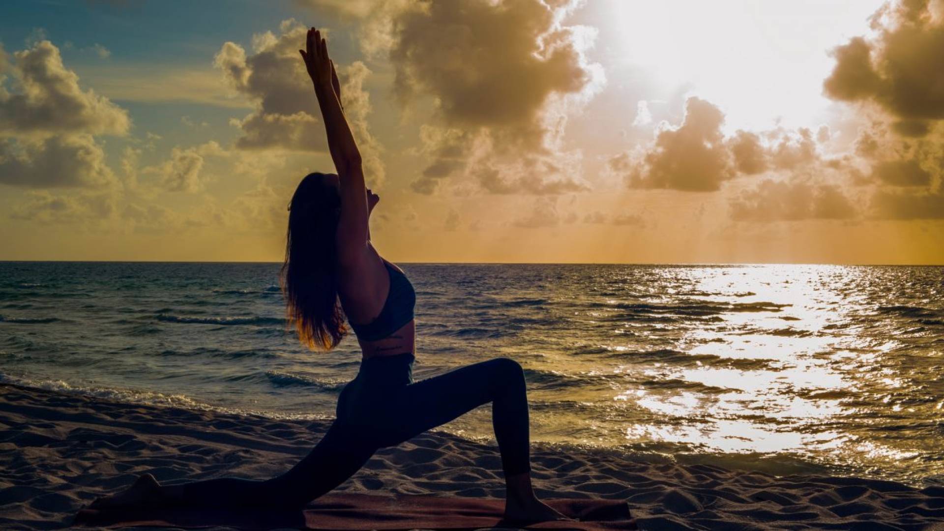 Woman doing yoga on beach overlooking the ocean at sunset