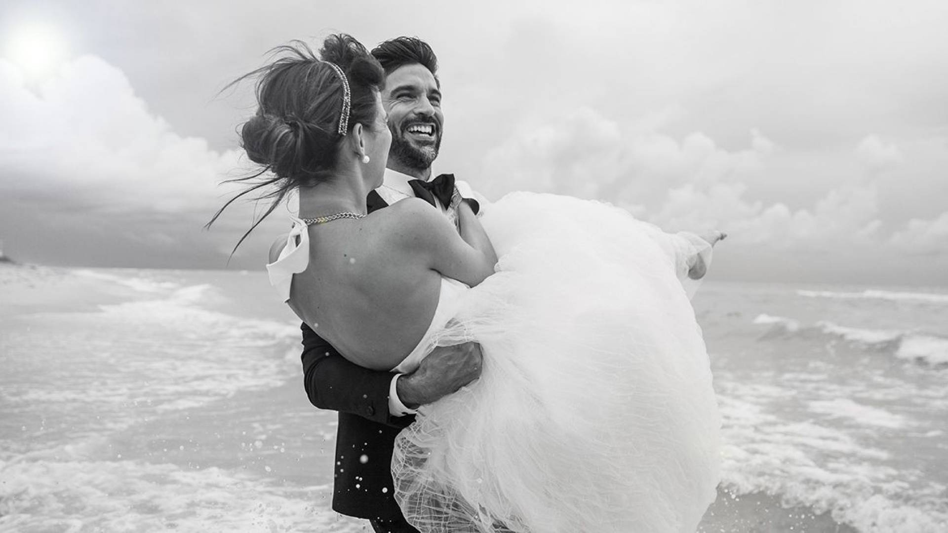 groom carries bride on the beach