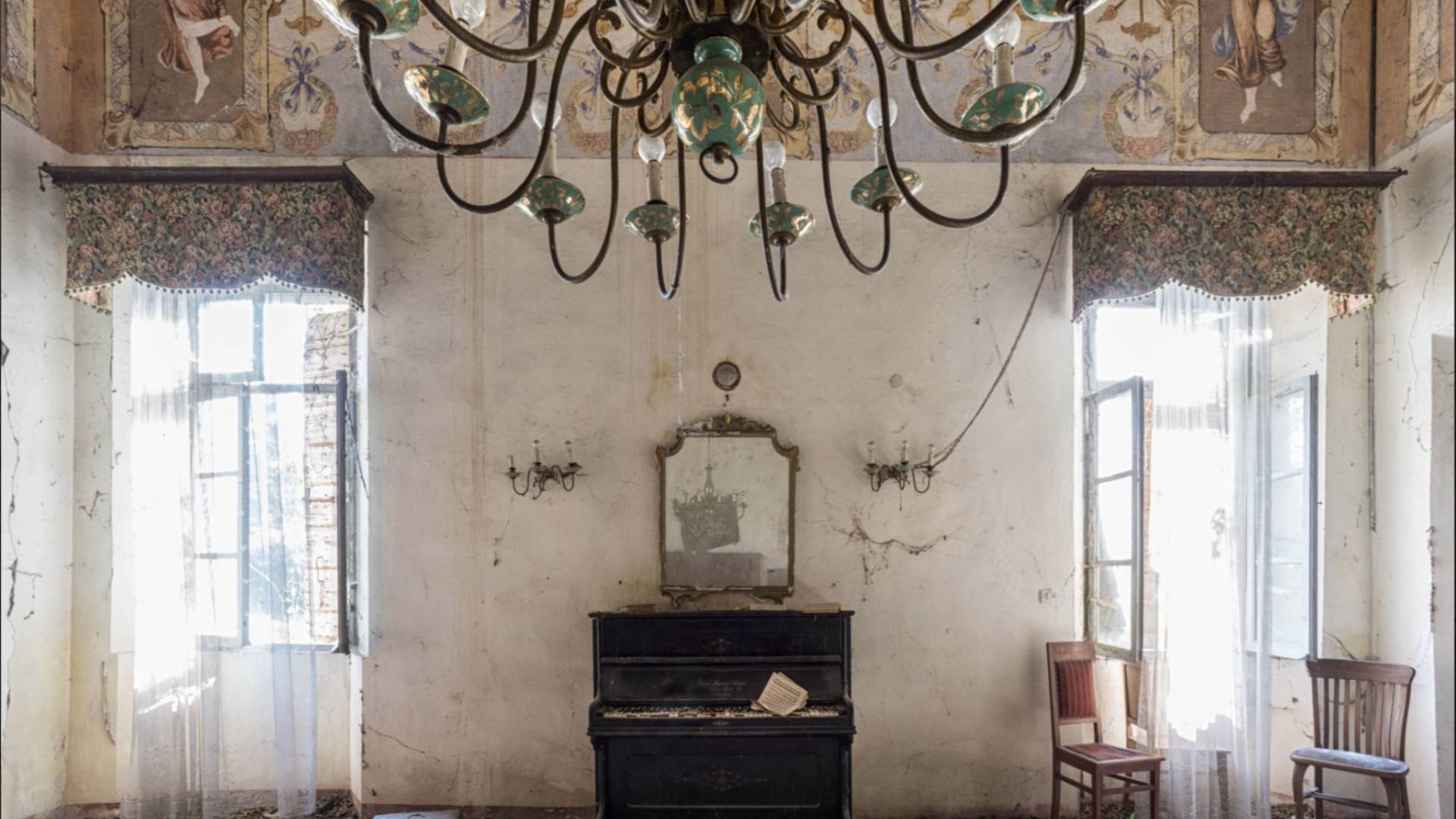 Piano sits in abandoned room with chandelier.