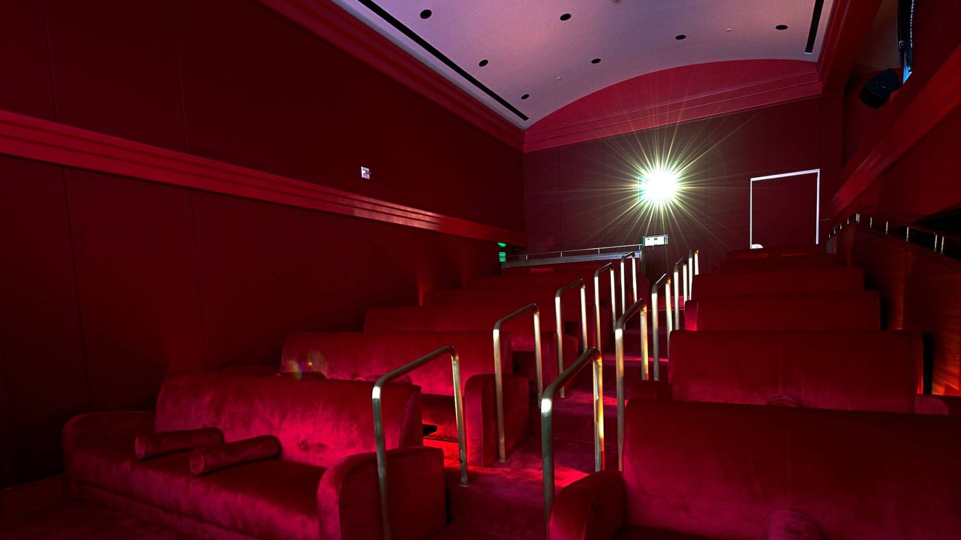 red velvet stairs and movie-theatre style seating with gold handrail with light from projector in background