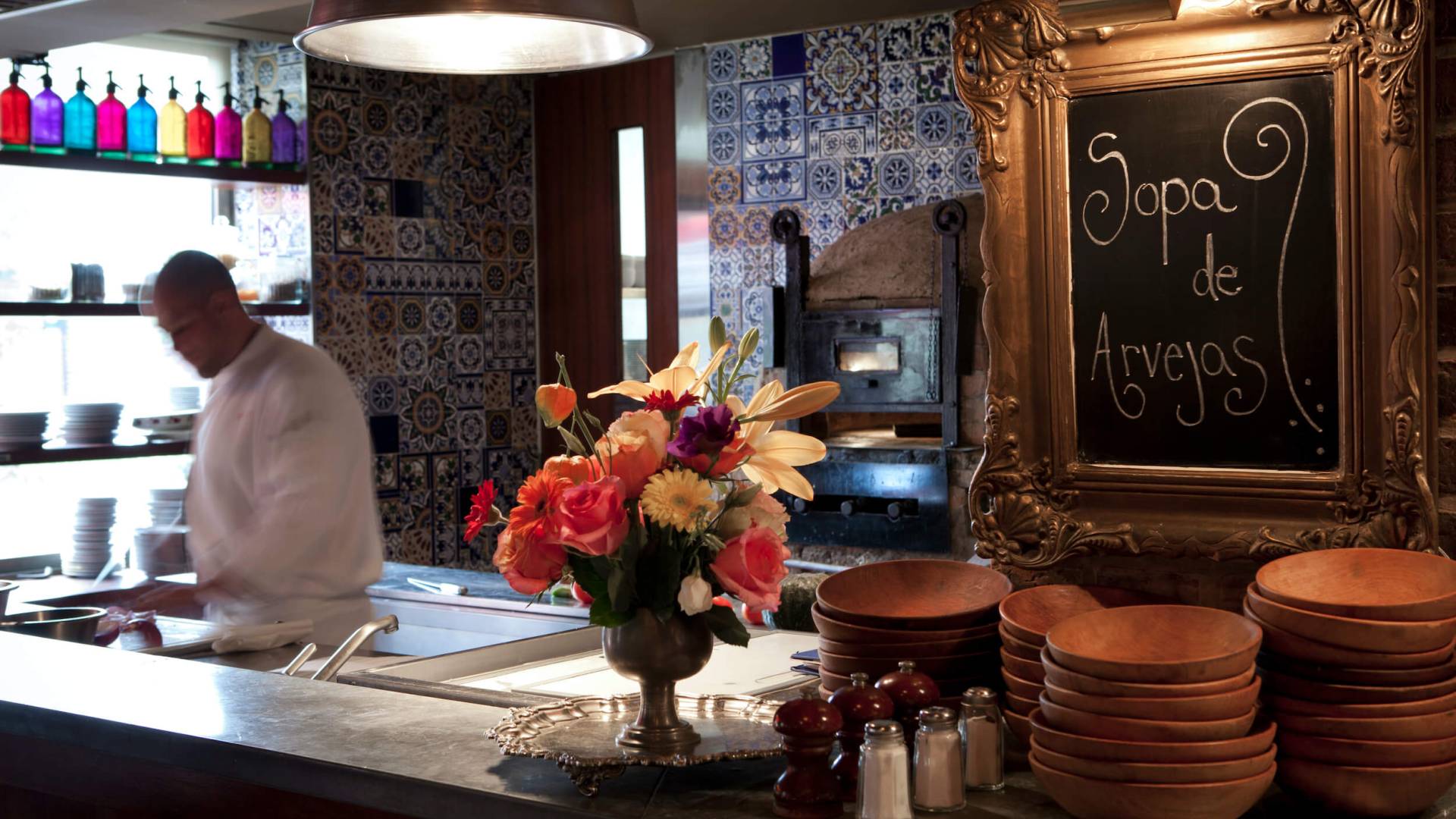 server scoops ladle of food into dish behind bar with flowers and chalkboard sign