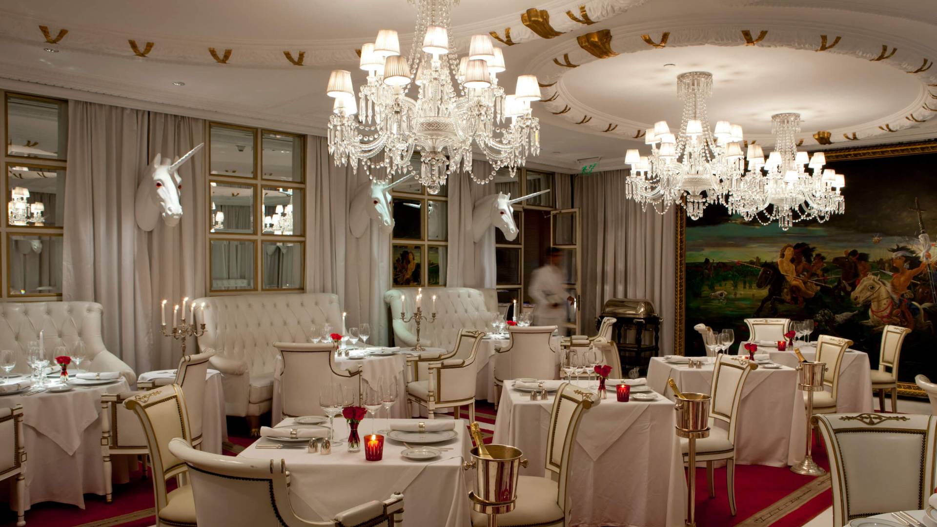 grand dining room with three chandeliers, unicorn heads on walls, red carpet, and white booths, tables, and chairs