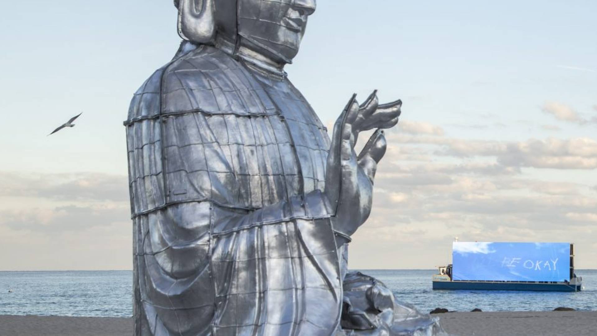 buddha statue with hand lifted sits in front of ocean