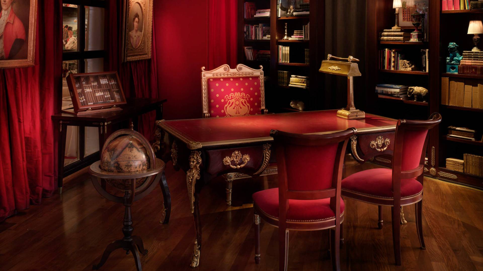 red chairs sit at desk with gold lamp and globe beside shelves full of books