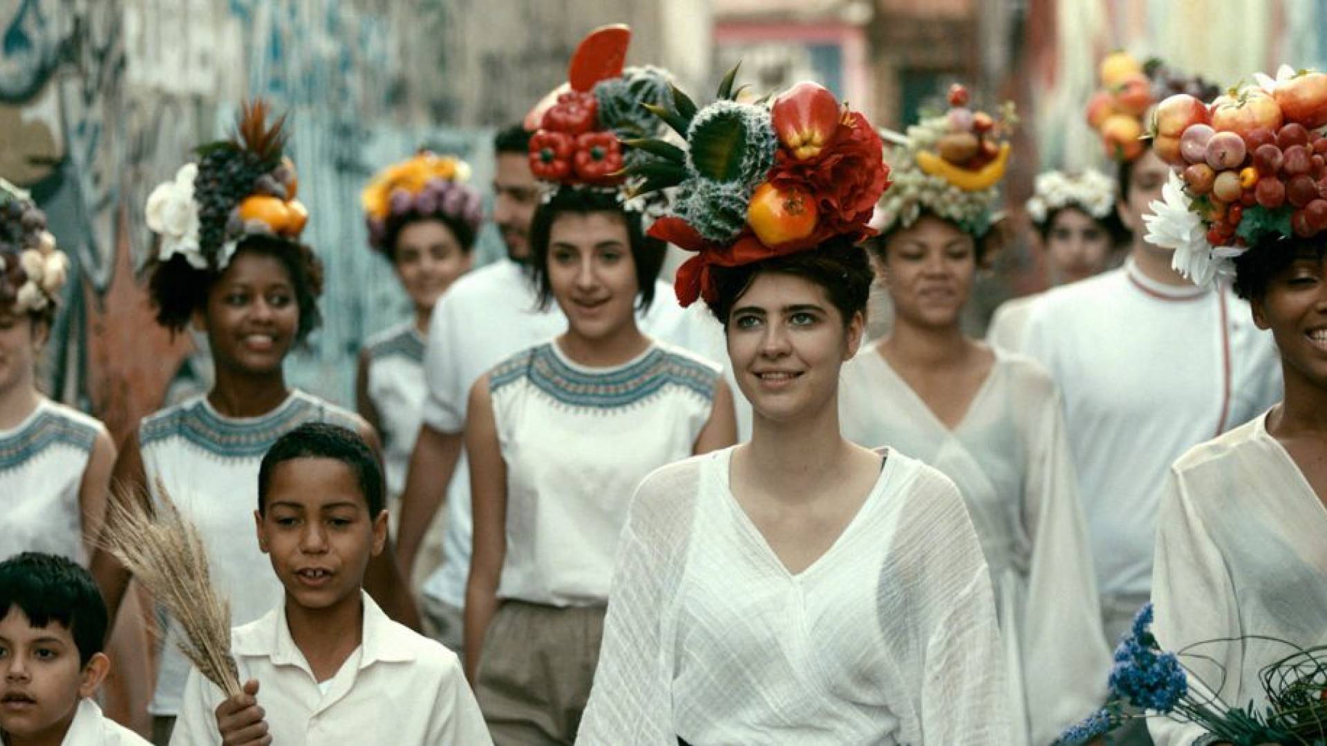 group of people with fruit on their heads walk toward camera