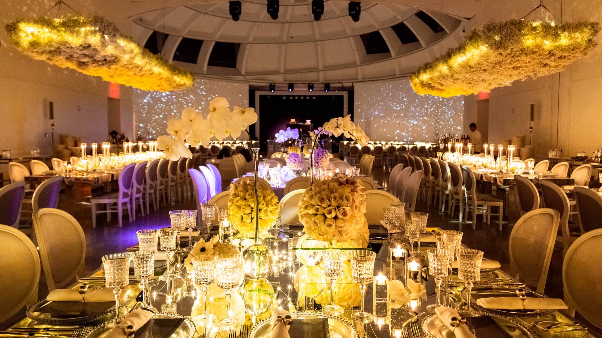gold lit table setting with innumerable chairs and candles