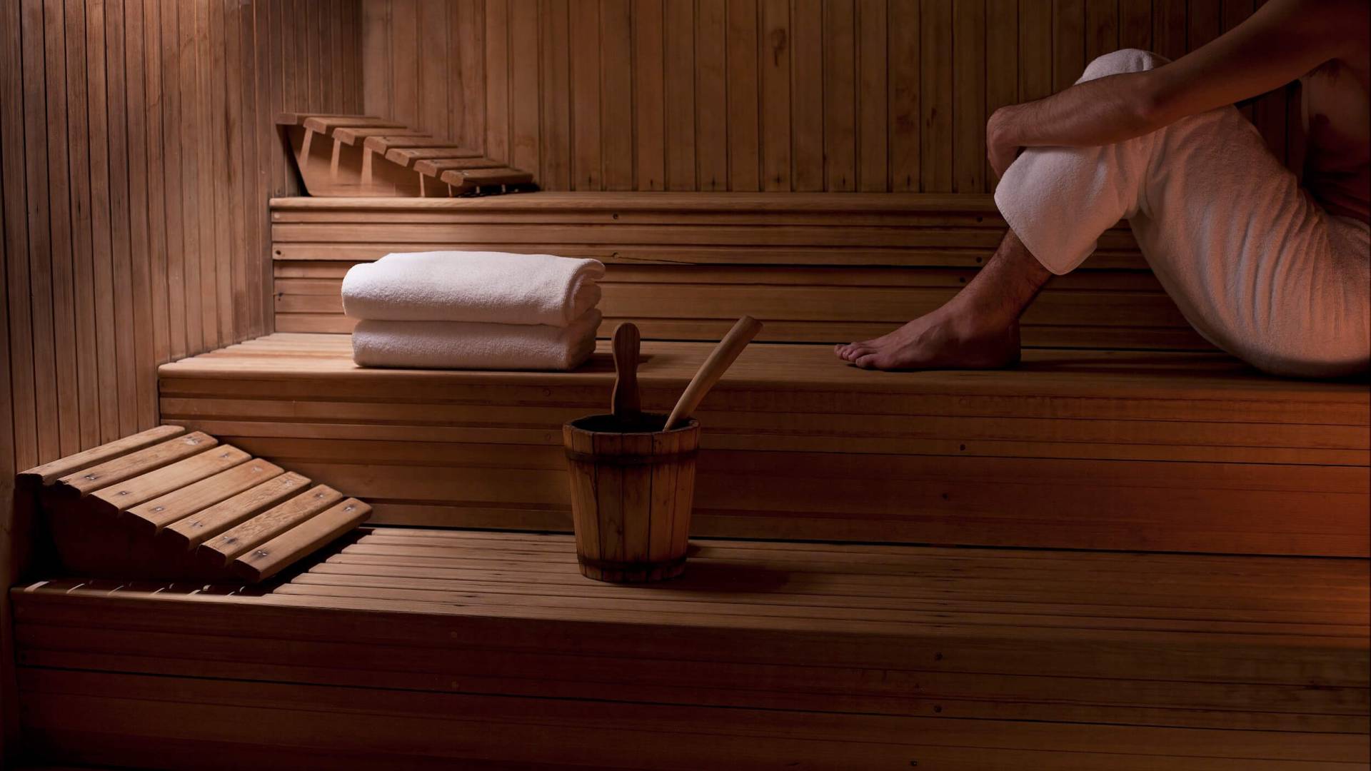 person sits in wooden sauna with towels sitting beside their feet
