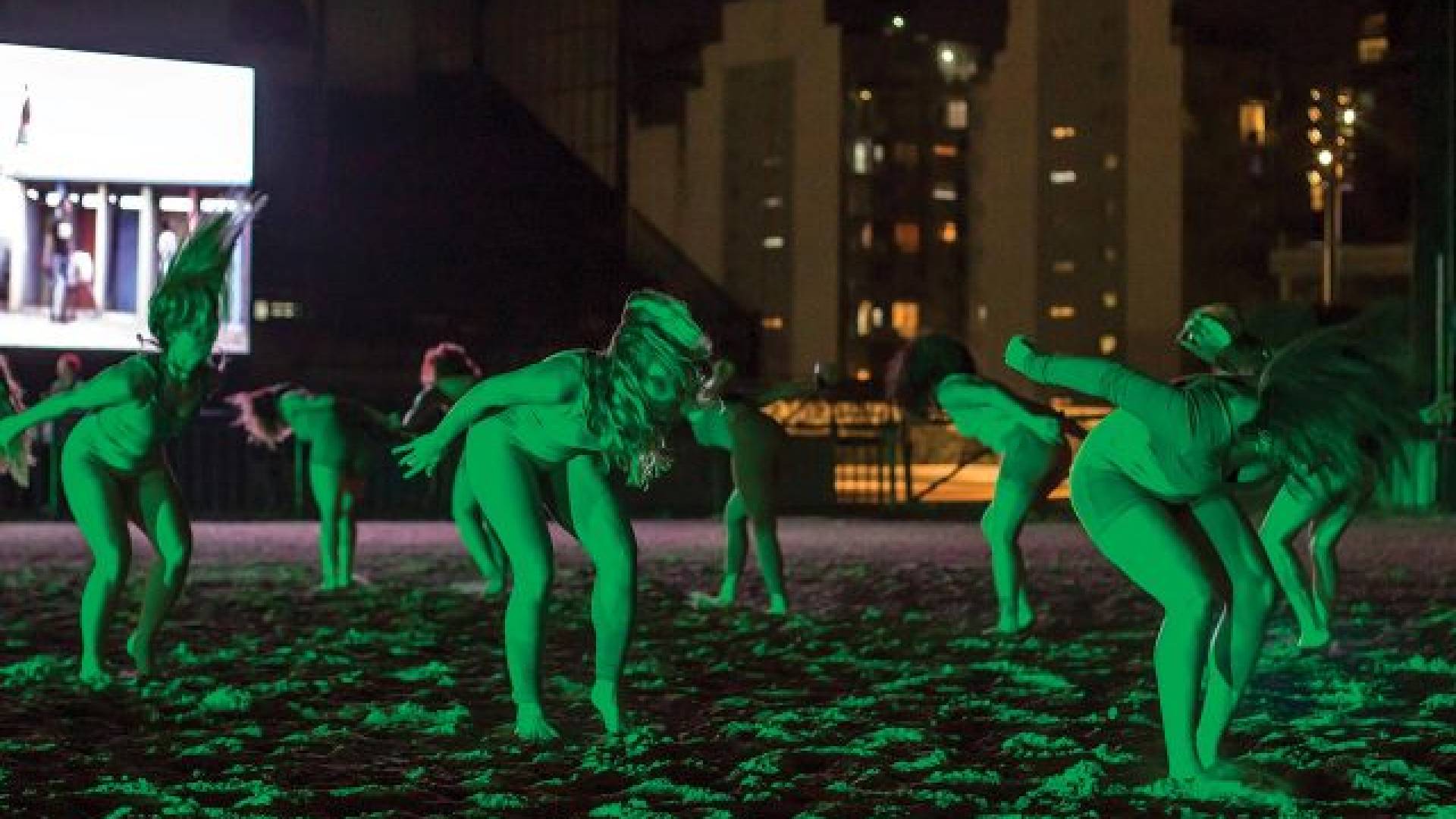 group of performers glow green as they're bent over mid-performance