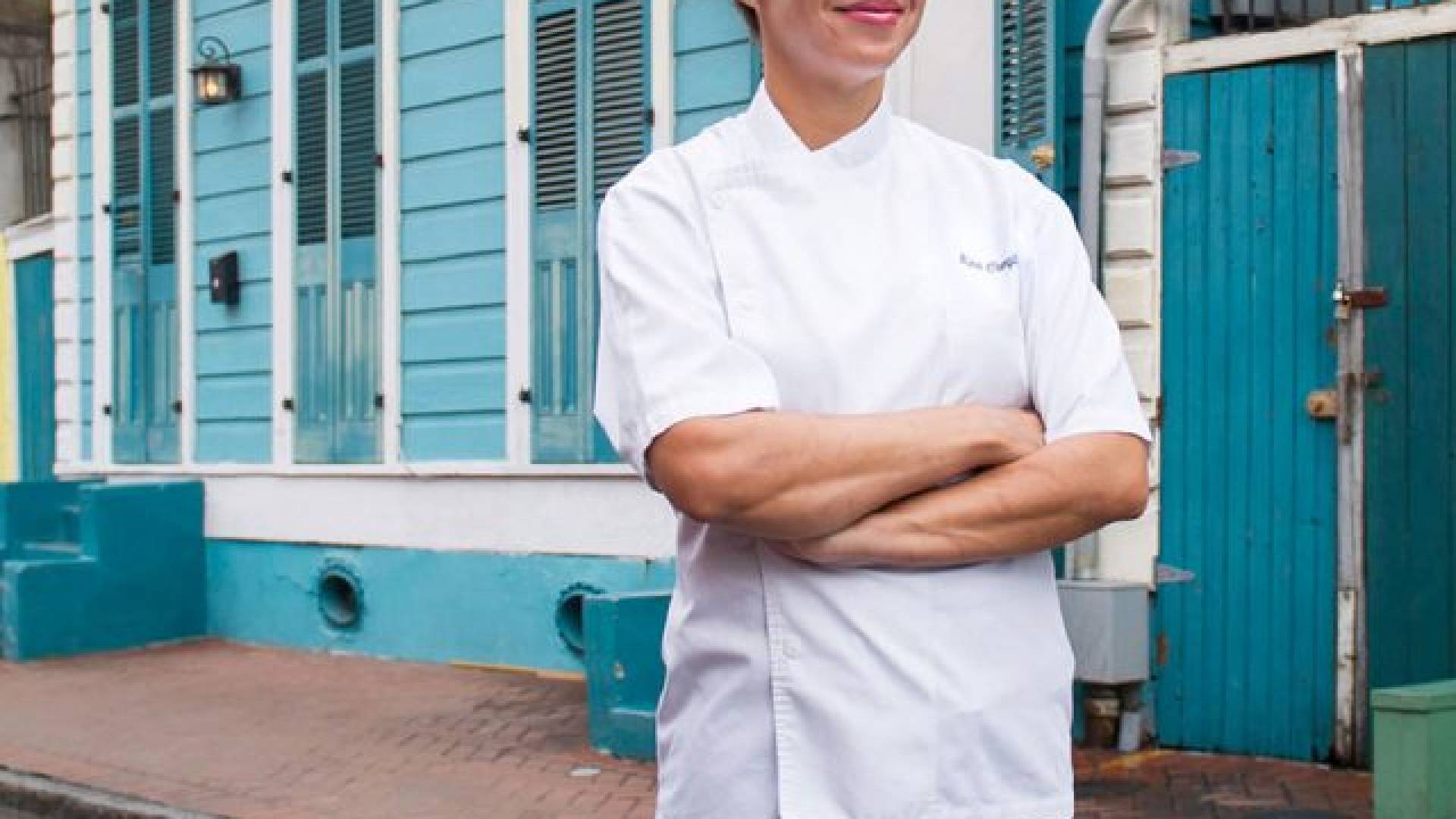 woman with arms crossed stands in street wearing chef's coat