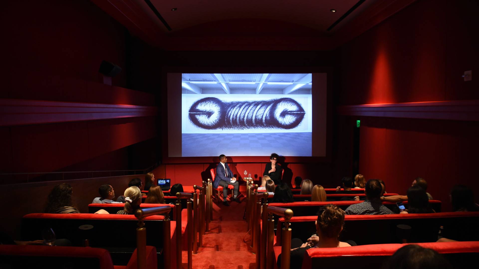 interior shot of performance in screening room with people in seats and projection on screen