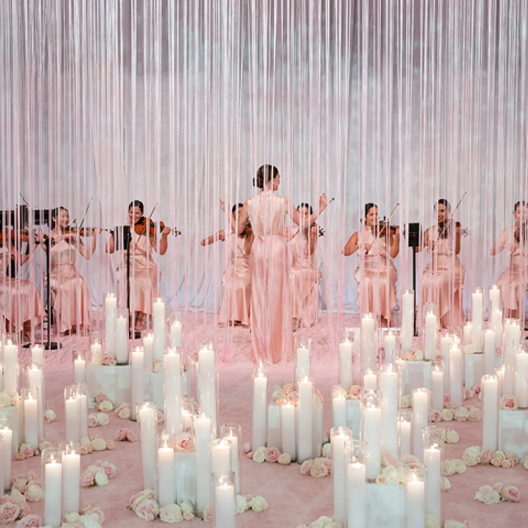 women playing violins behind a curtain of rope amongst candles