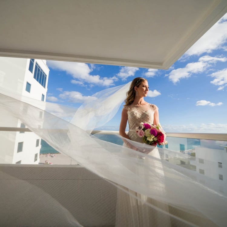 bride stands on balcony with veil flowing in the wind