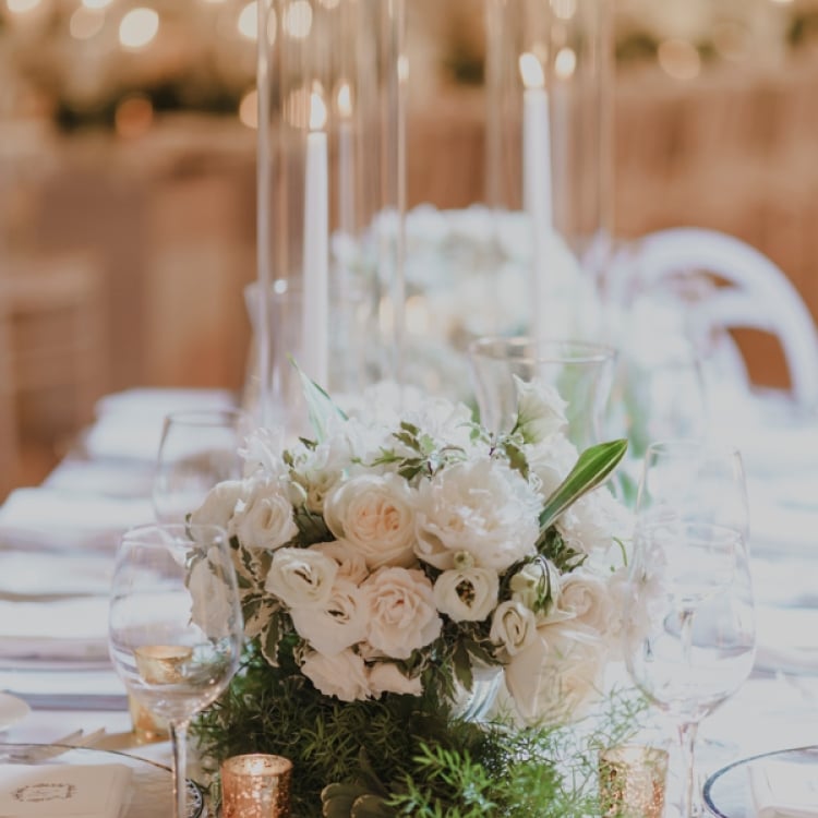 White floral arrangement with tall glass incased candles as center pieces on white table