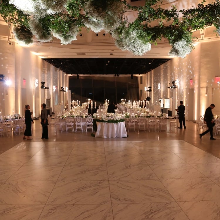 interior of wedding venue with floral and greenery on ceiling and staff mingling amongst stables 