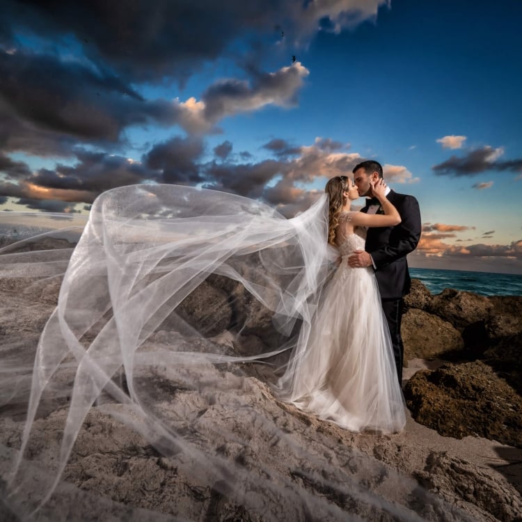 bride and groom kiss on rocks beside the ocean