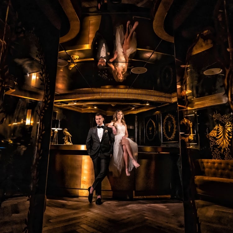bride and groom sit on a bar in dimly lit room with a golden hue