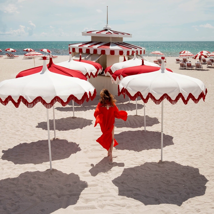 woman walking on the beach surrounded by white and red umbrellas