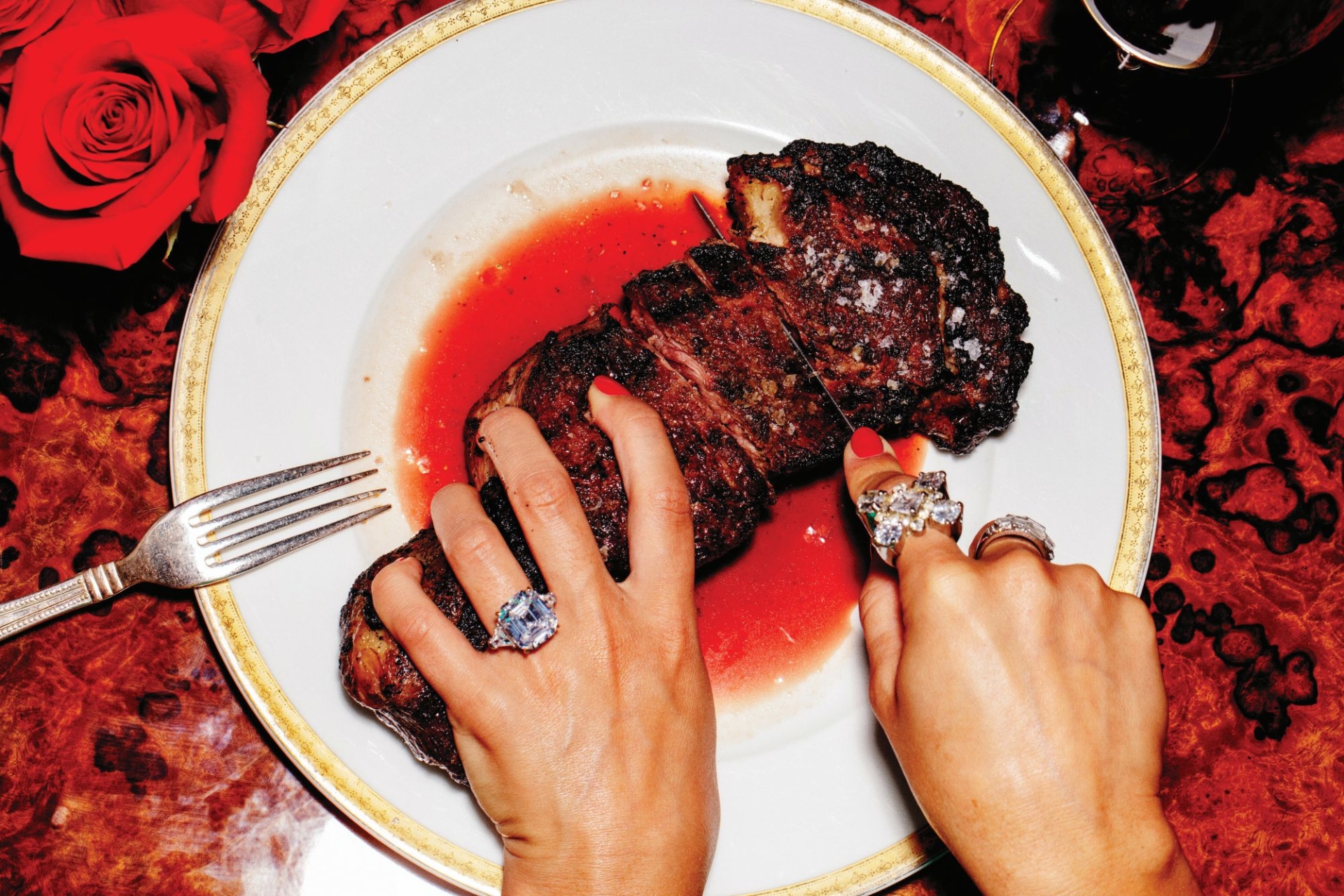 A woman in rings holding and cutting a piece of meat