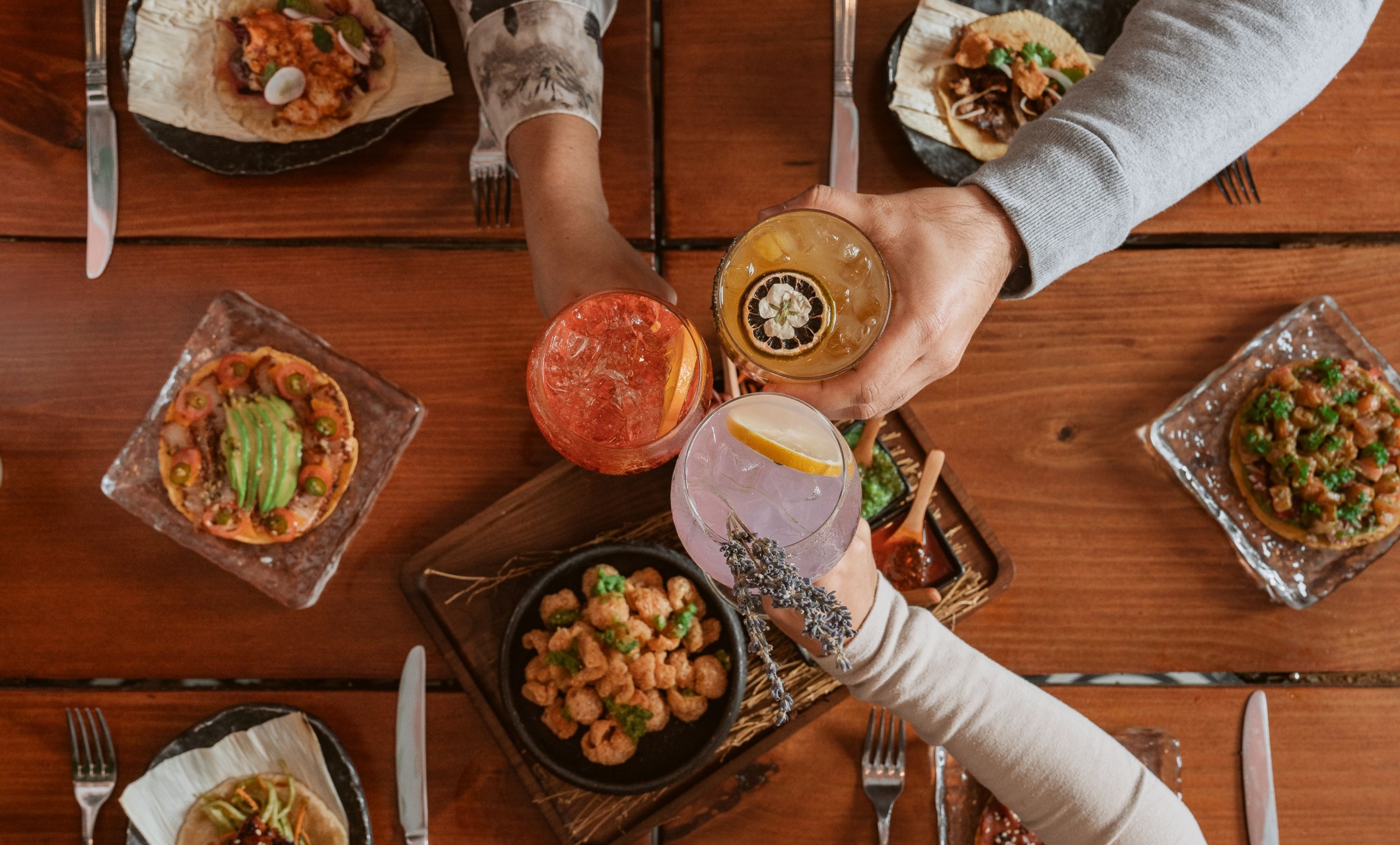 Overhead view of friends toasting with cocktails over a wooden table of shared plates at Faena Hotel 