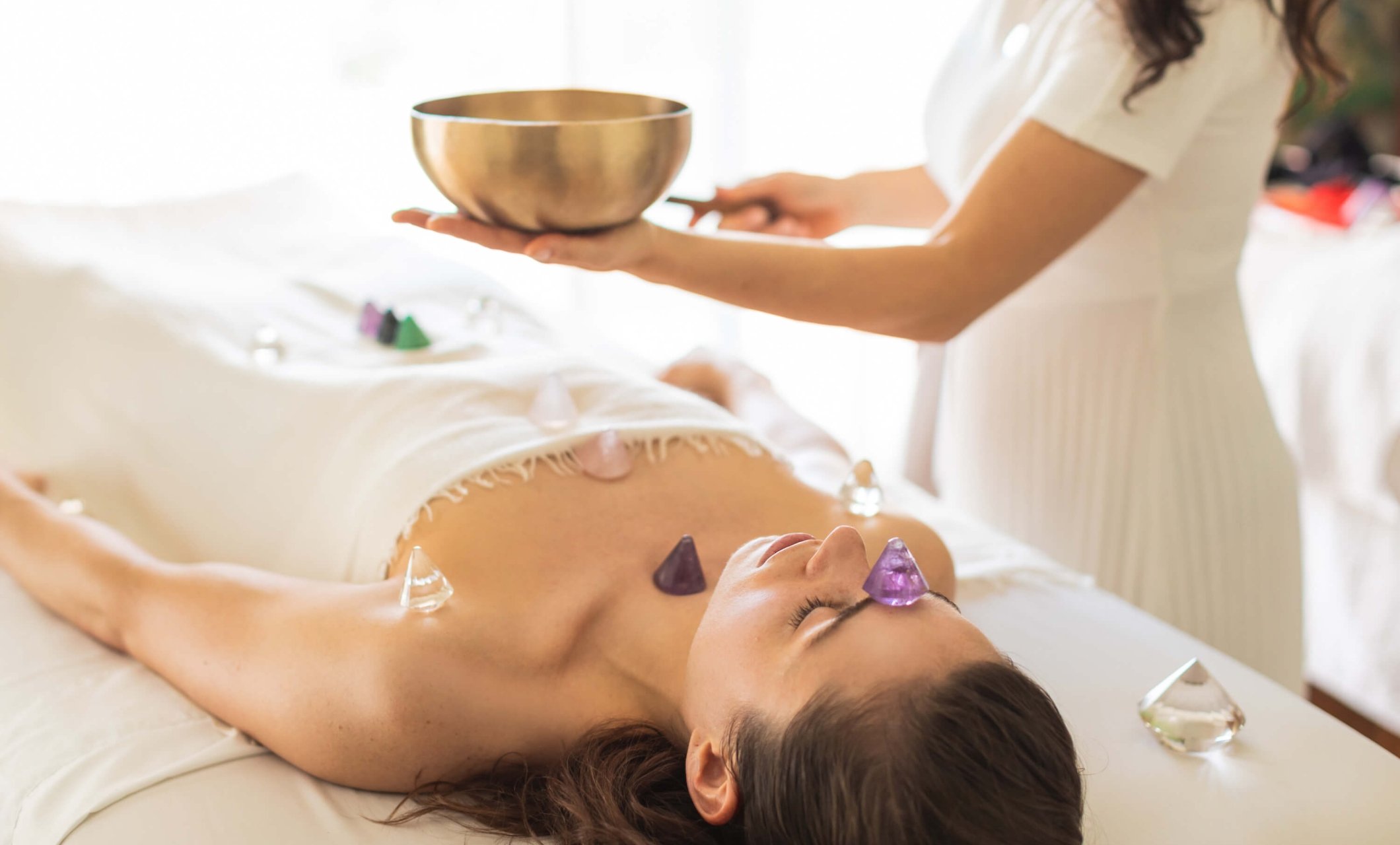 woman lays on table receiving crystal treatment by spa worker