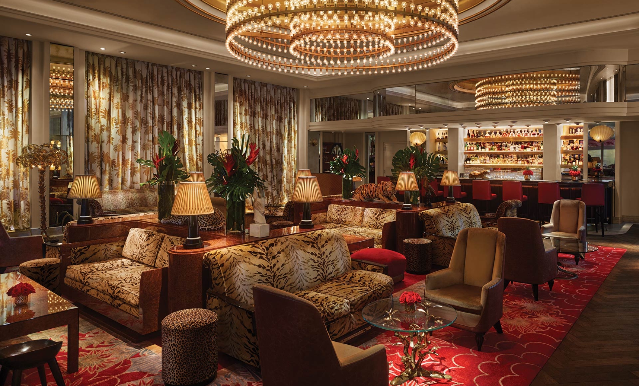 A luxurious lounge with a bar, sofas, armchairs, and a large chandelier.