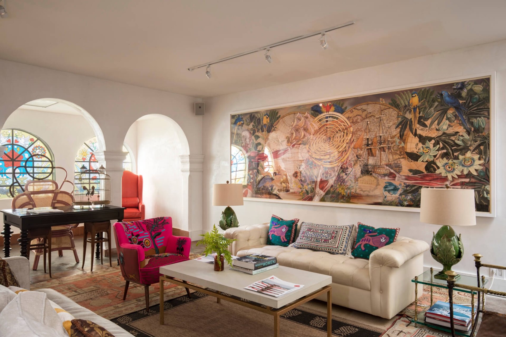 red chair and white couch sit in room with painting on wall and items sitting on side tables