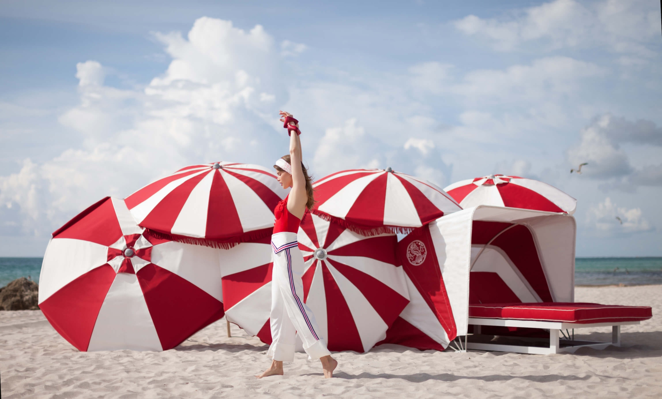 woman walking on the beach in front of red and white umbrellas
