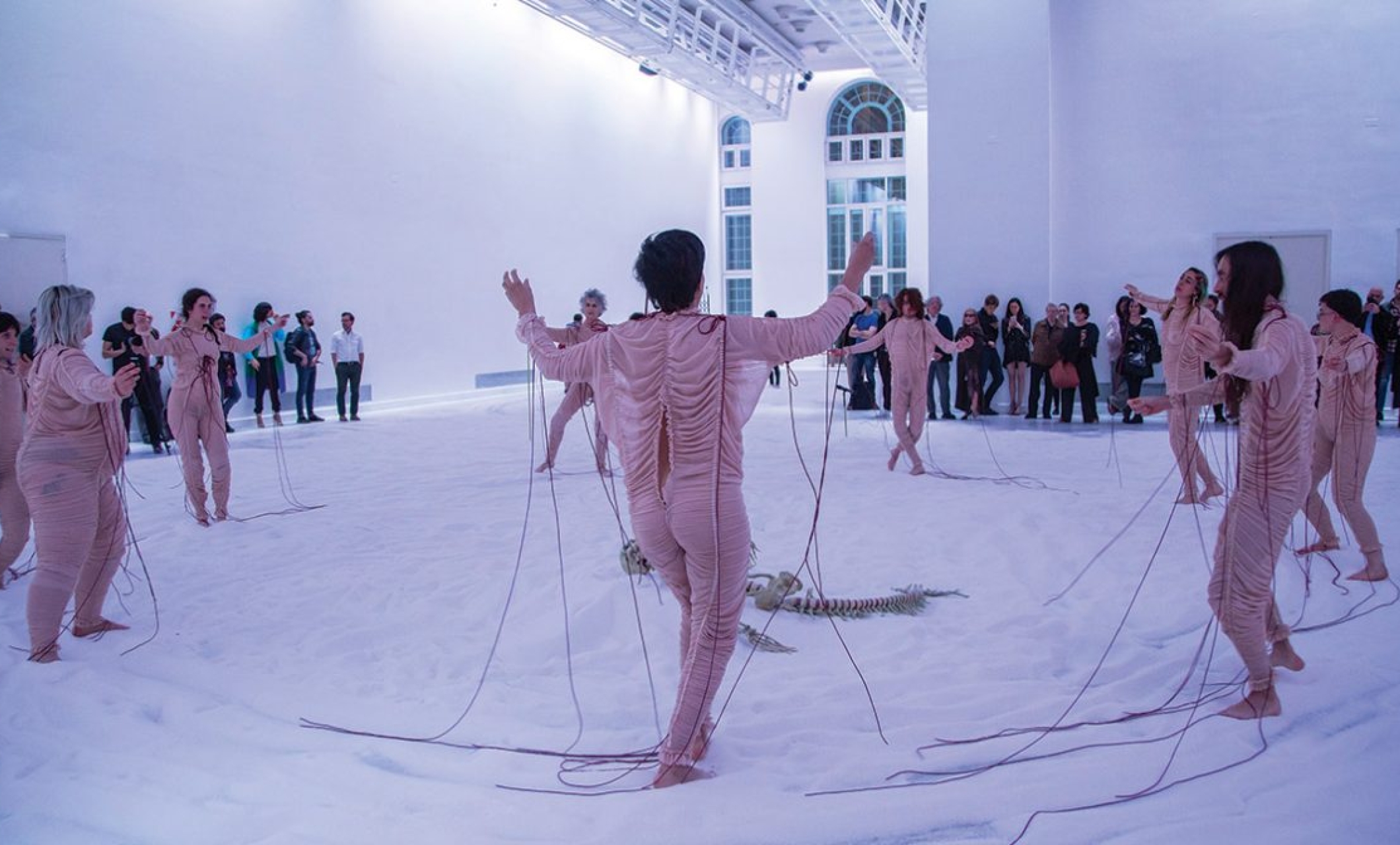 performers dressed in pale pink skin tight fabric dance on white cloth covering the floor