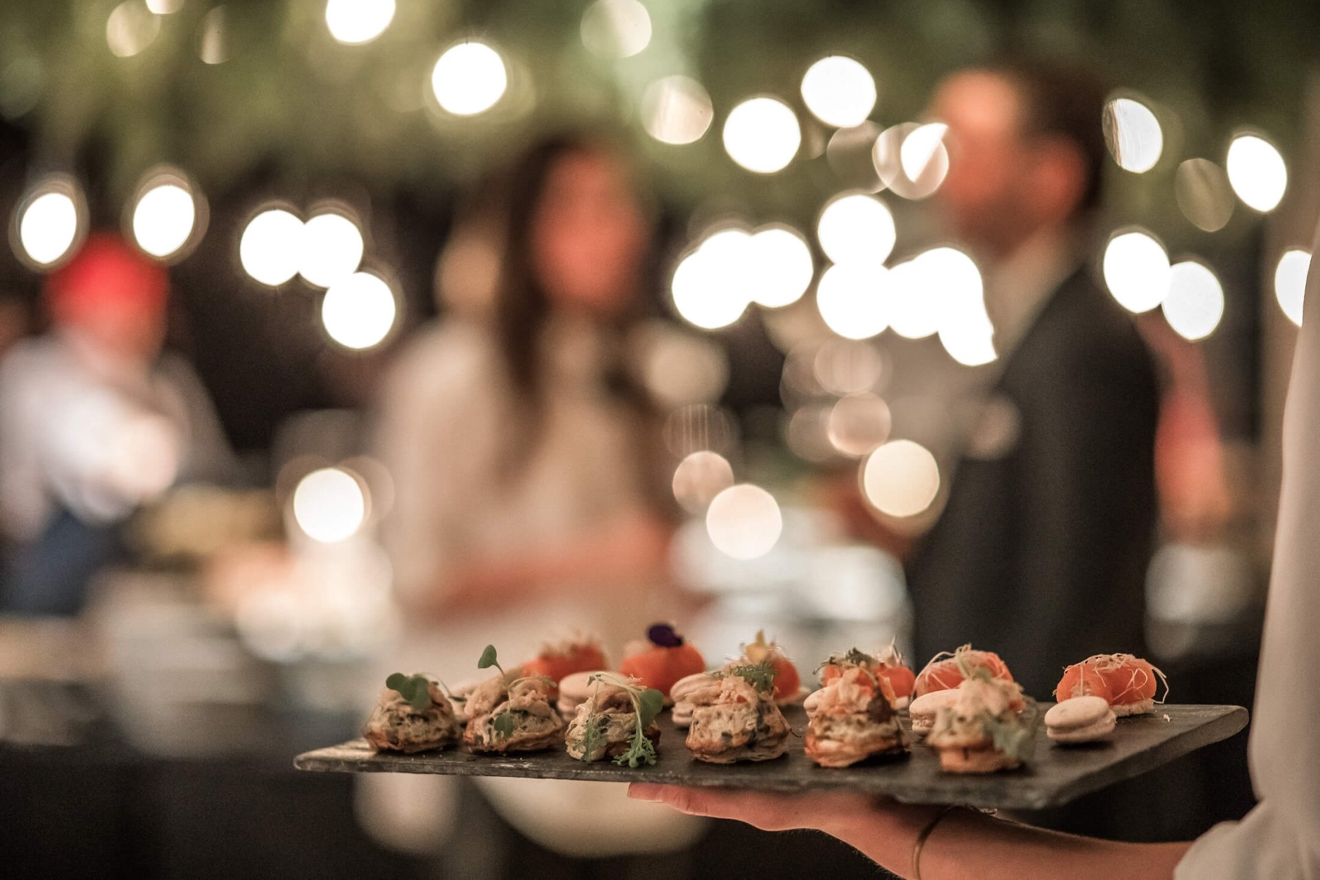 server with slate tray of appetizers walks toward two people blurry in background