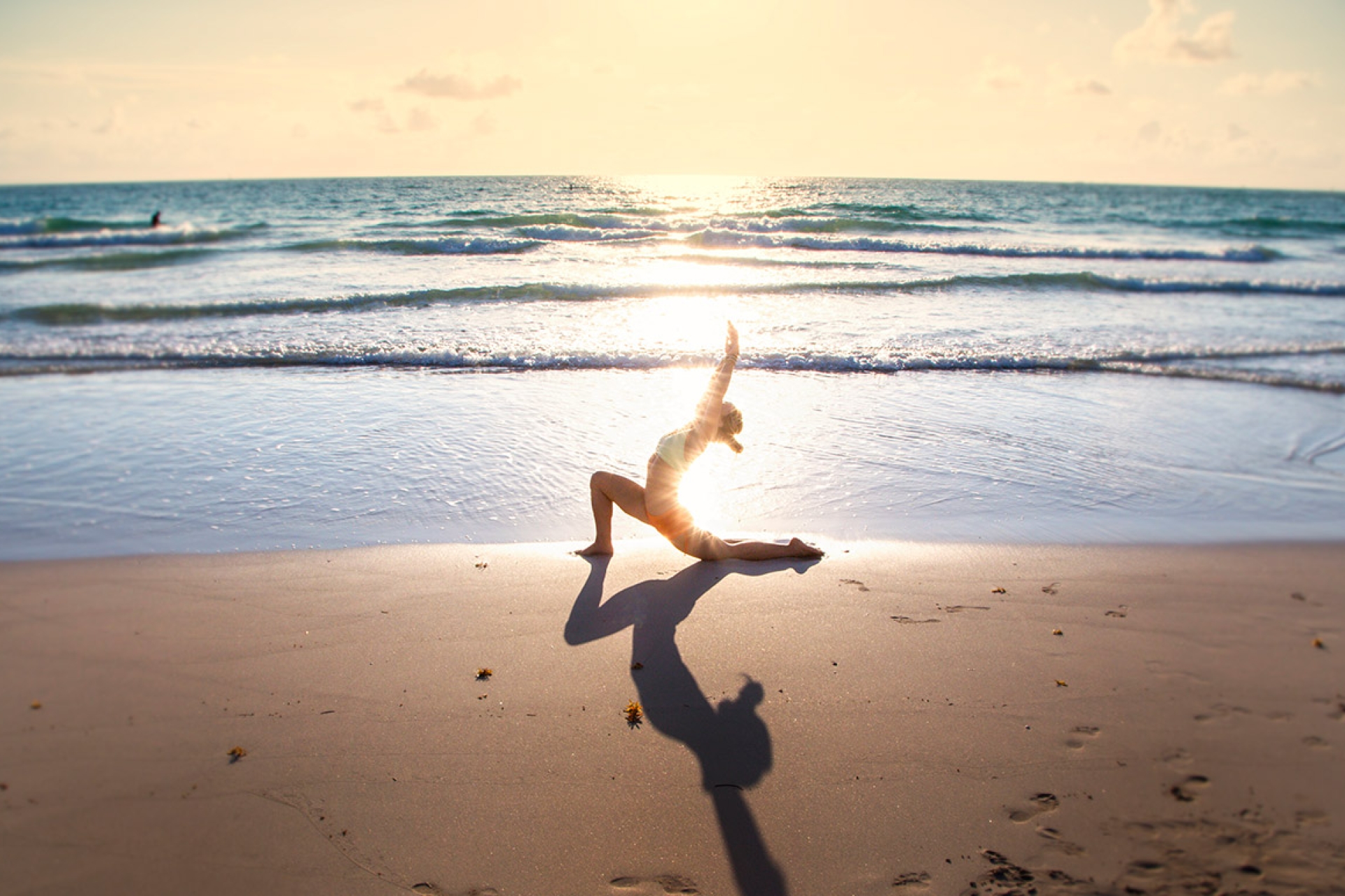 woman performs yoga stretch on beach with sunset in background