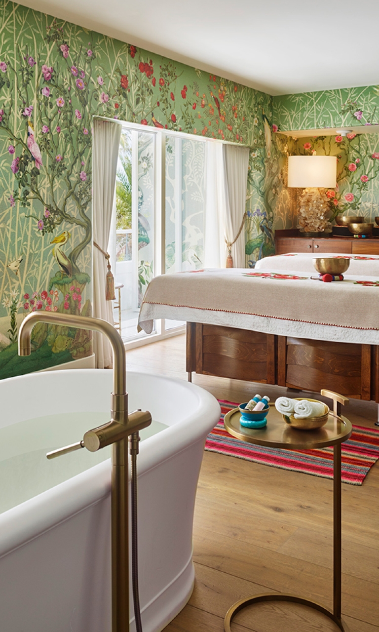 A spa room with a freestanding bathtub, massage table, and floral wallpaper.