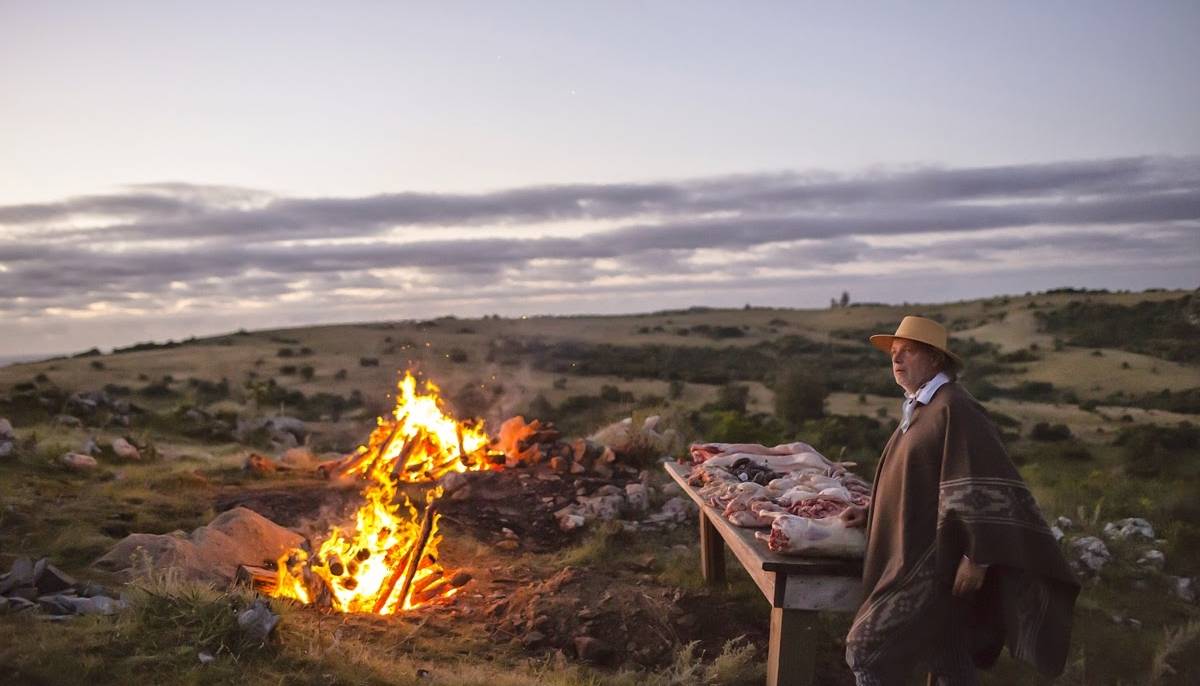 francis mallmann on a hillside cooking meat over an open fire