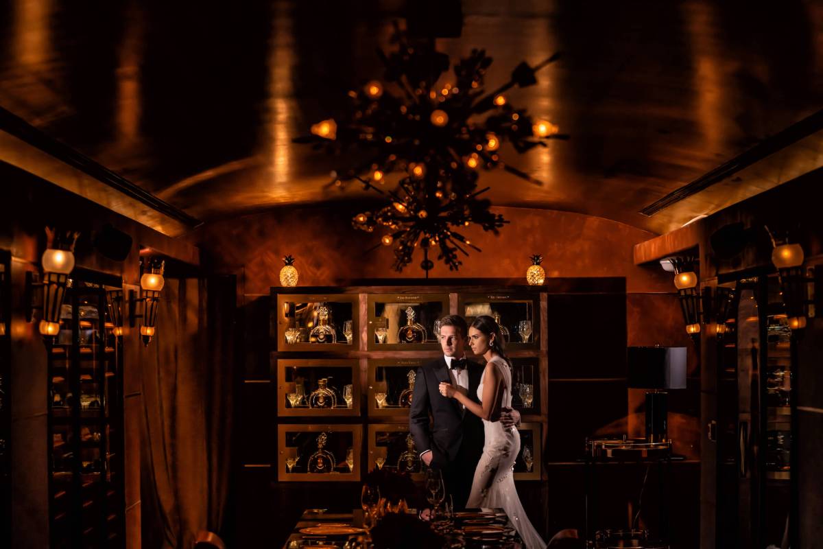 bride and groom stand in dimly lit room with a golden hue