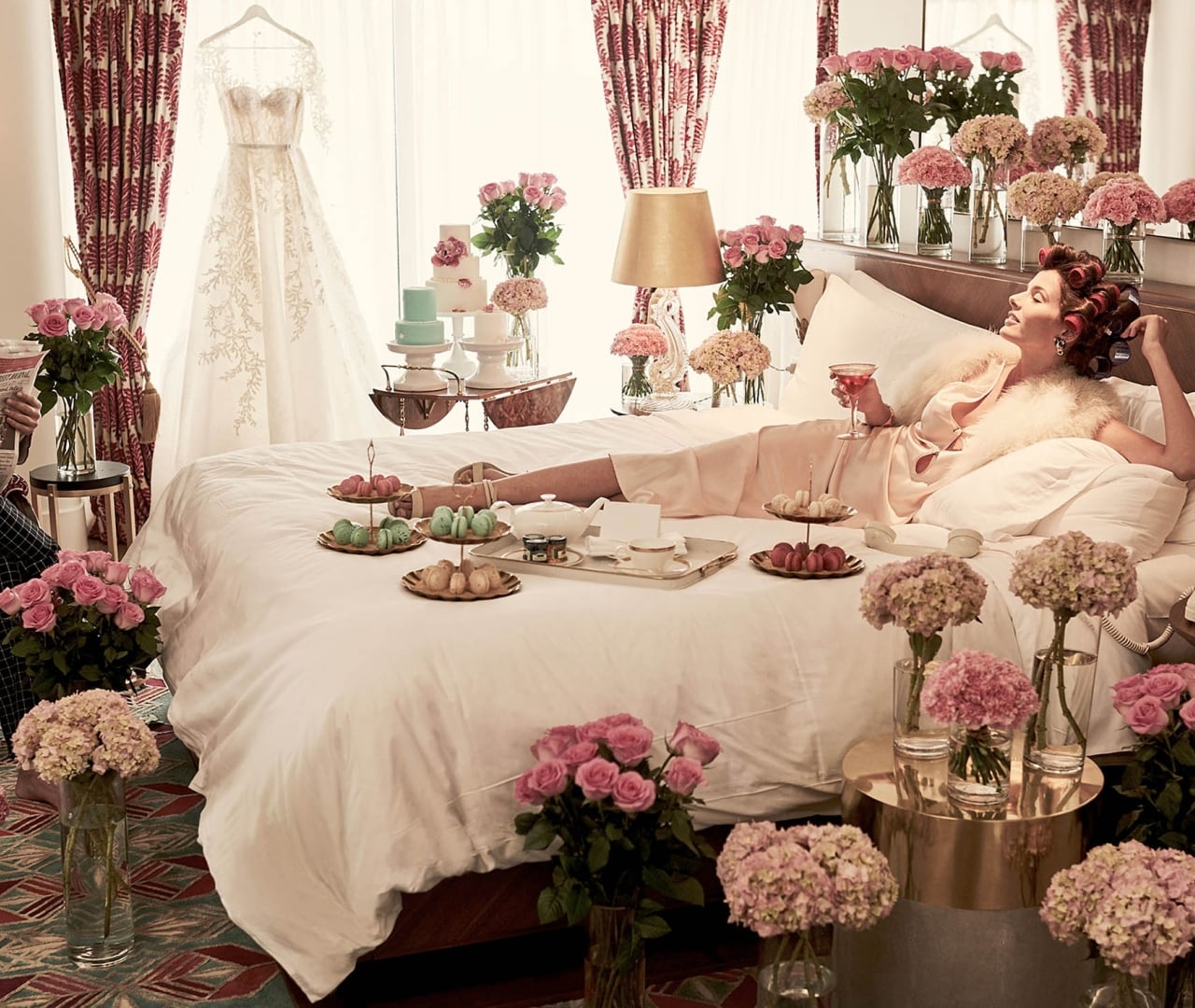 A woman in a luxurious room with a bed, flowers, food, and a wedding dress