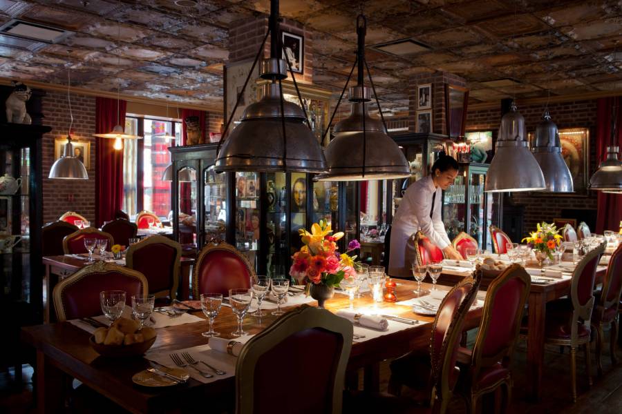 server sets table in room with tin ceiling, large light fixtures, and red chairs framed in gold