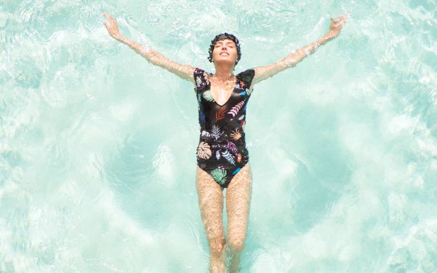 woman in one-piece bathing suit and matching swimcap floats on her back in light blue water