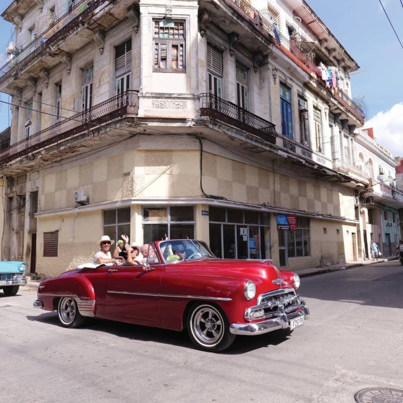 A group of friends driving around Cuba in an old red car