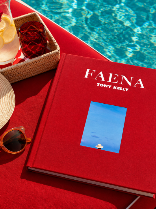 Red Faena coffee table book by the pool, styled with a straw hat, sunglasses, and a refreshing drink.